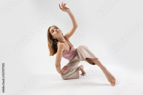 Young beautiful slim girl dances contemporary on a beige studio background