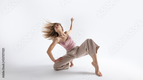 Young beautiful slim girl dances contemporary on a beige studio background