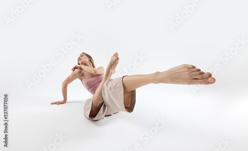 Young beautiful slim girl dances contemporary on a beige studio background