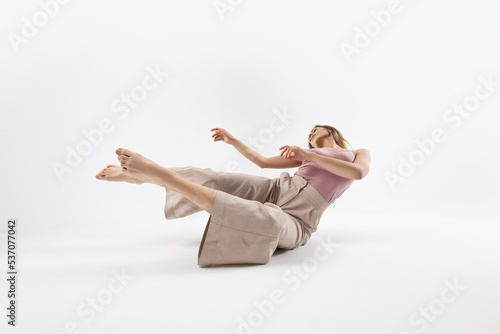 Young beautiful slim girl dances contemporary on a beige studio background
