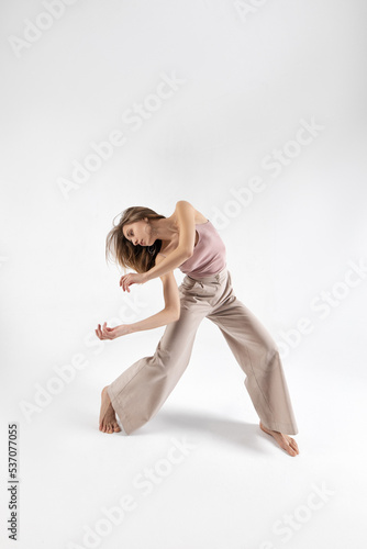 Young beautiful slim girl dances contemporary on a beige studio background