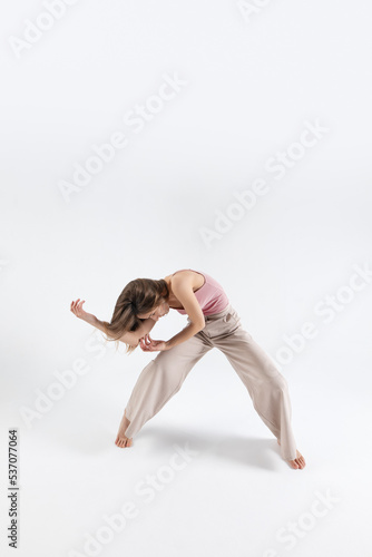 Young beautiful slim girl dances contemporary on a beige studio background