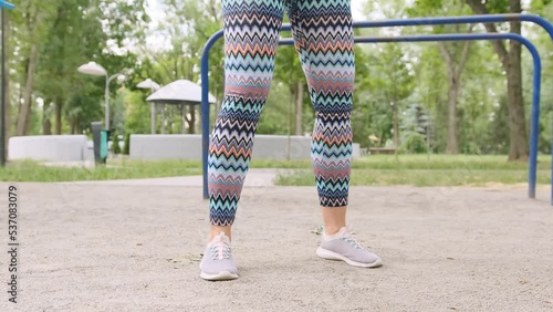 Pretty girl doing squats outdoors. Young woman exercising outside and make buttoms workout photo