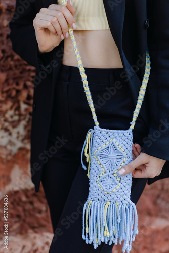 A woman in a black suit holds a knitted phone case in Ukrainian colors with macrame on the street. Close up