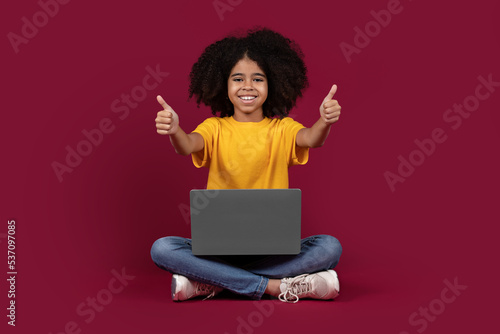 Happy african american child using laptop, showing thumb up © Prostock-studio