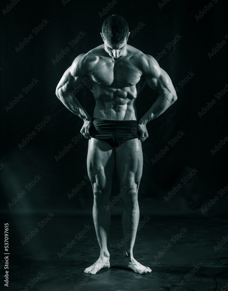 Handsome bodybuilder doing classic double biceps pose, looking away, on dark background