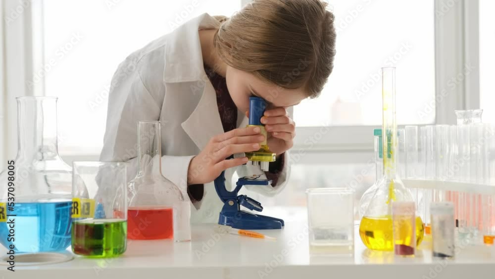 School girl looking at test results through microscope in chemistry class. Female pupil studying in lab