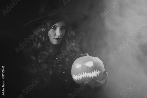 Valokuva Mysterious black witch with steaming pumpkin as head of jack-o-lantern on dark backdrop