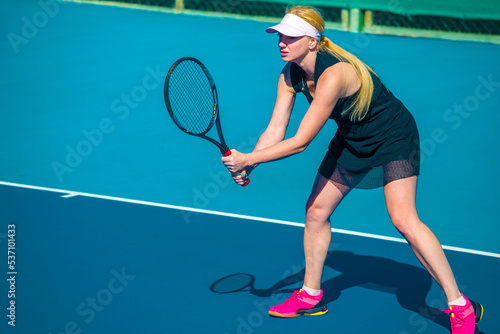 A girl plays tennis on a court with a hard blue surface on a summer sunny day © Павел Мещеряков