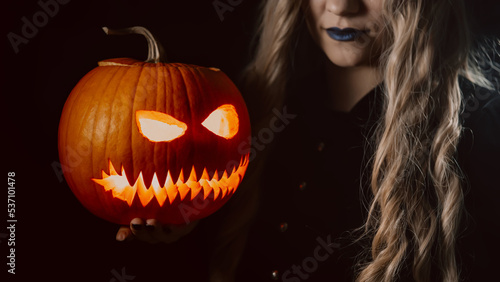 Fotografie, Tablou Mysterious black witch with pumpkin as head of jack-o-lantern on dark backdrop