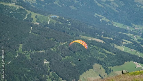 Man paragliding with a wide parachute in the sky with light wind in the beautiful forest green alps mountains landscape. Extreme sport athletes, free-falling through the air, base jumping, sky diving  (ID: 537101818)