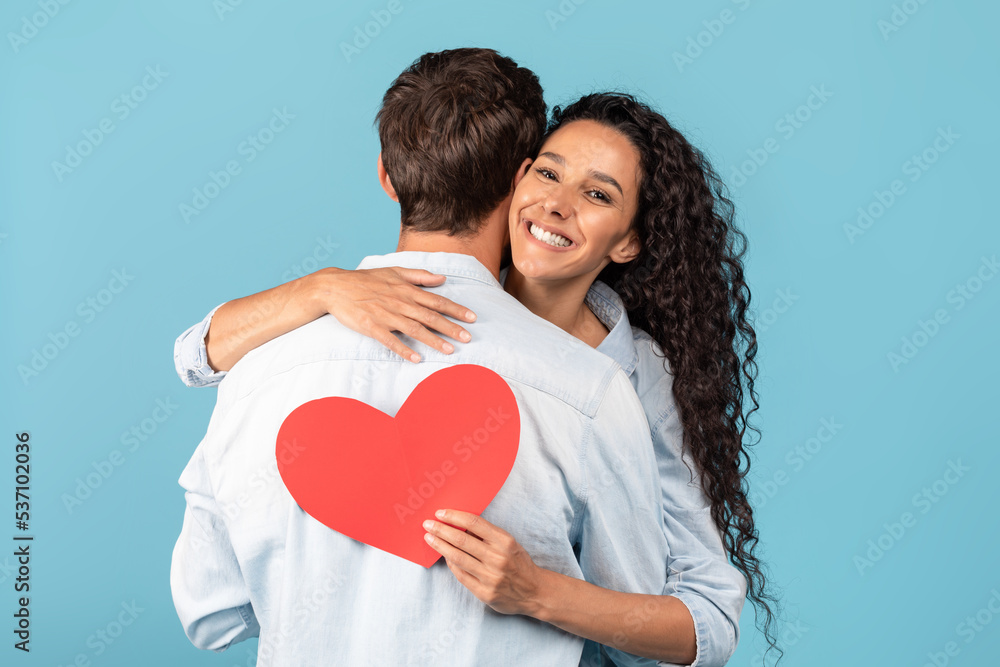 Glad young middle eastern woman hugging man, holding heart, celebrate anniversary