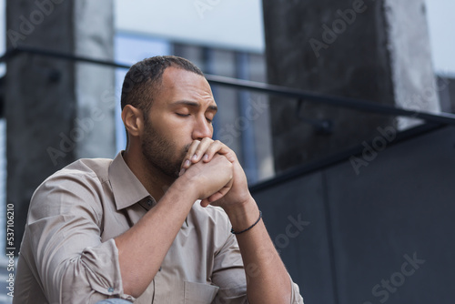 Close-up photo portrait of upset office worker fired businessman in depression, man with closed eyes sitting on stairs of office building outside.