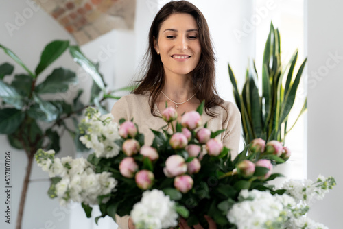 Positive woman holding a huge bouquet of flowers in her office. Birthday present smile.