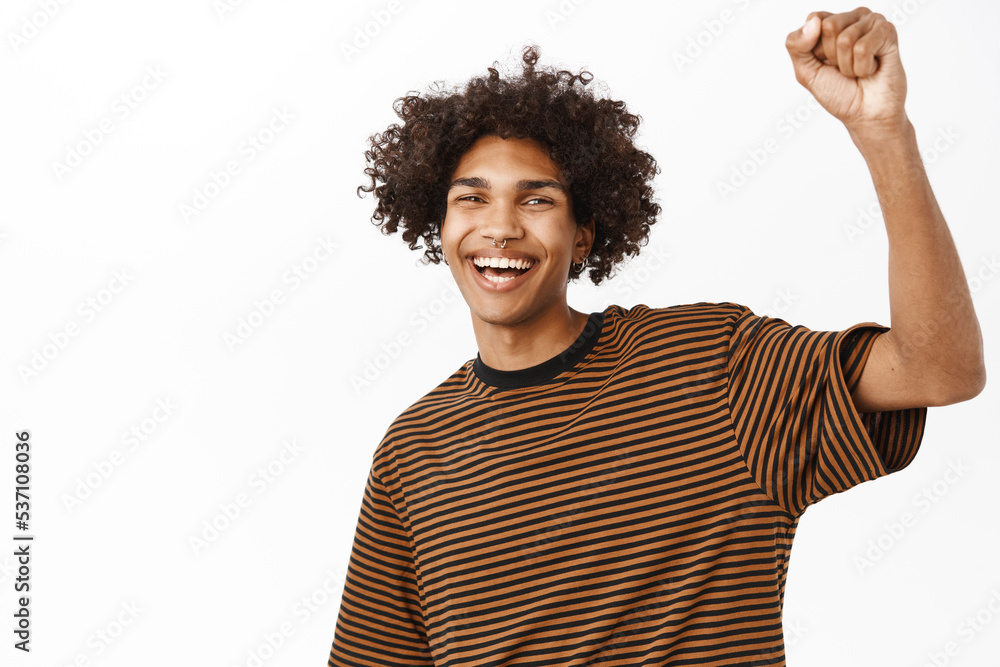 Enthusiastic boy raising one hand and cheering, chanting in support, young activist protesting, standing over white background Enthusiastic boy raising one hand and cheering, chanting in support, young activist protesting, standing over white background