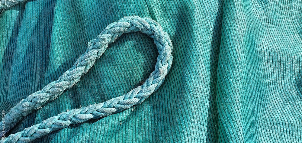 Marine rope and fishing net. Blue rope. Turquoise background. Turquoise fishing net and rope. Fishing gear. Blue cord on a blue background.
