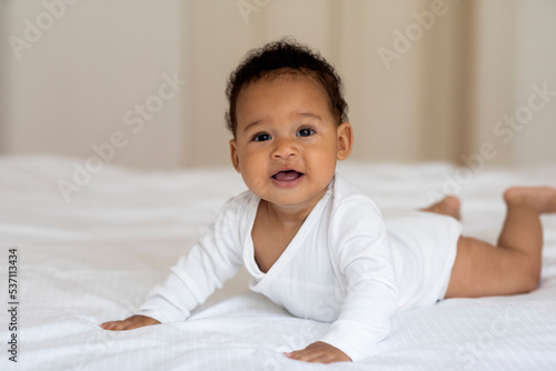 Childcare Concept. Adorable Little African American Baby Crawling On Bed At Home