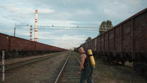 Young muscular man with a balloon drager on his back is training on the railway sidings next to a factory with chimneys photo