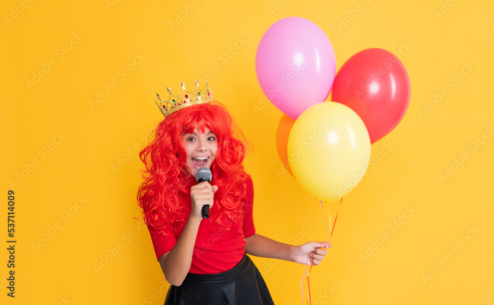 glad child in crown with microphone and party balloon on yellow background glad child in crown with microphone and party balloon on yellow background
