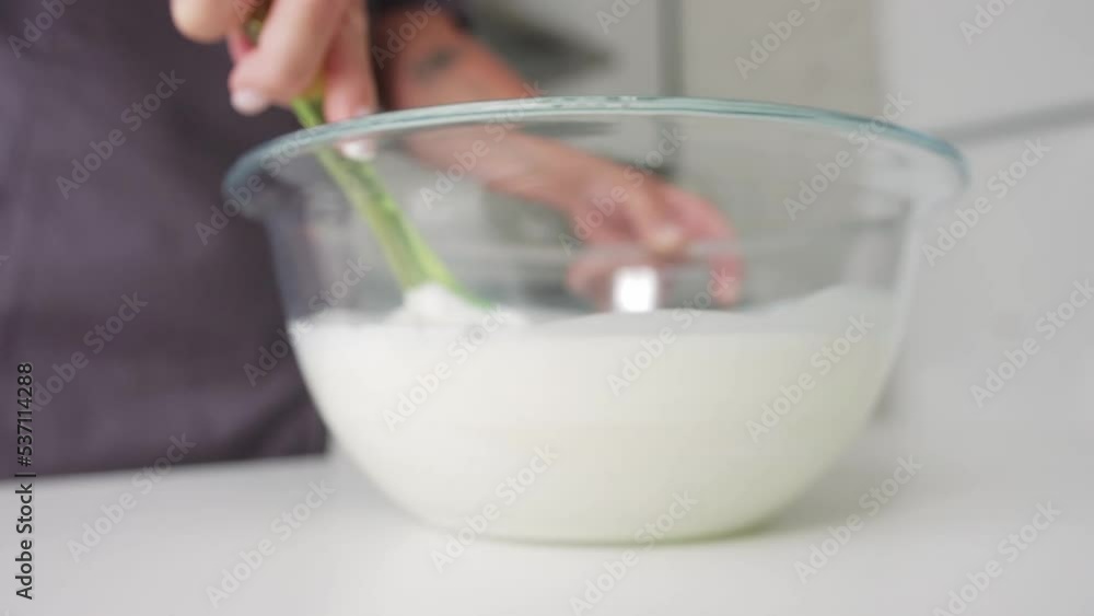 Woman baker mixing white vanilla cream in the glass bowl