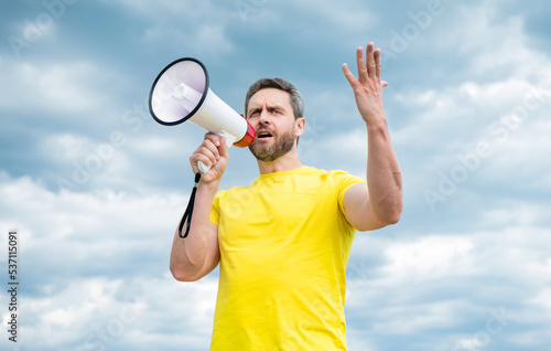 man in yellow shirt speaking in loudspeaker on sky background © be free