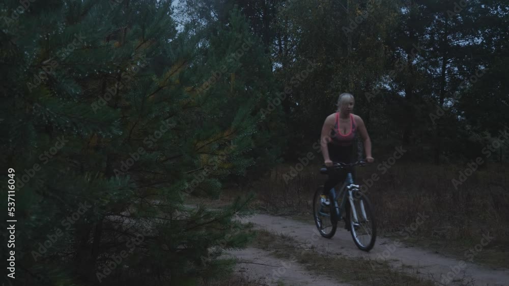 Athletic young woman rides a bike fast. A blonde woman in sportswear rides a mountain bike along a forest path in the evening. The concept of a bike ride through the forest. Athletic young woman rides a bike fast. A blonde woman in sportswear rides a mountain bike along a forest path in the evening. The concept of a bike ride through the forest.