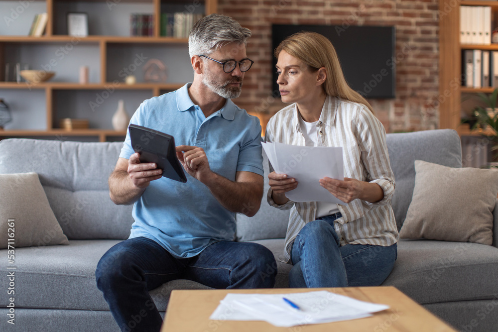 Worrying busy sad middle aged european lady with documents and male with tablet work with bills Worrying busy sad middle aged european lady with documents and male with tablet work with bills