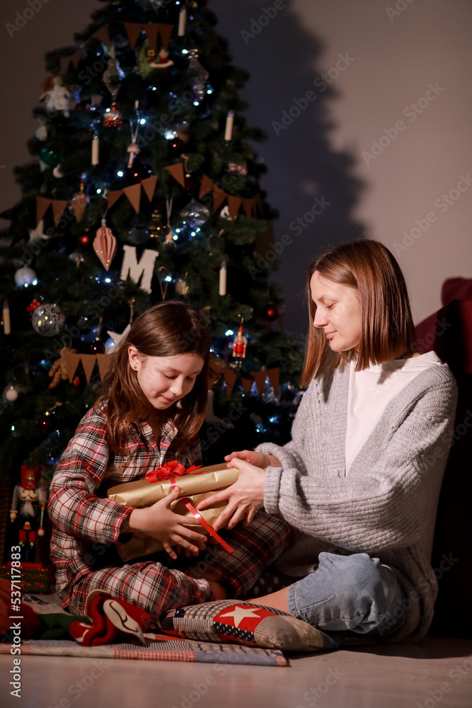 young mother and daughter open Christmas Lighting Present Gift Box front of Xmas Tree. Happy Mom with kid girl in Magic Night. Family merry christmas and new year holiday concept. High quality photo
