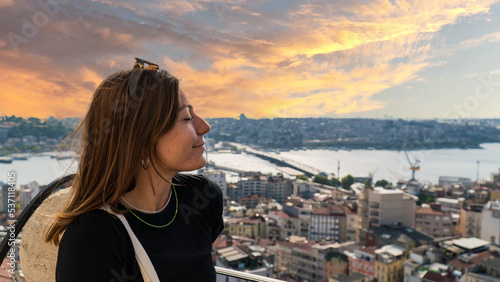 Fototapeta Naklejka Na Ścianę i Meble -  Young tourist woman sightseeing with Istanbul landscape at sunset. Young beautiful woman watching Istanbul from the Galata Tower