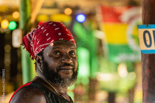Retrato horizontal de cerca del rostro de un hombre afrocaribeño de barba con un pañuelo rojo en su cabeza al aire libre sonriendo mirando a cámara. 