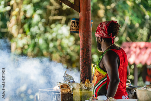 Imagen horizontal con vista desde atrás de un hombre afro caribeño con una pañoleta en su cabeza cocinando a la parrilla comida típica del caribe de Costa Rica