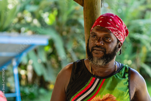 Retrato horizontal de un hombre afro caribeño de mediana edad con una pañoleta en su cabeza y de barba con canas recostado en un poste relajado photo