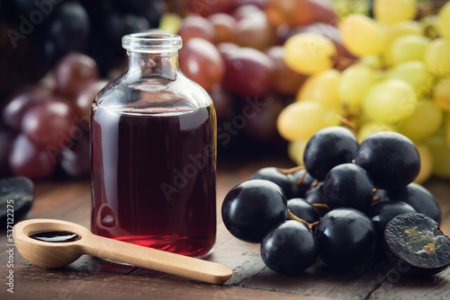 Bottle of grape molasses and scoop of grape syrup. Sweetener, cough medicine. Black, green and purple grapes on kitchen table. photo