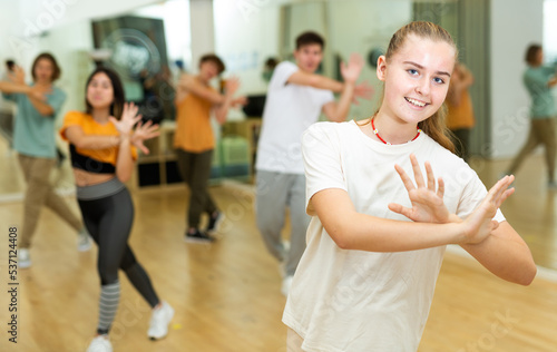 Cheerful teen girl enjoying while training movements of modern group dance in choreography class .