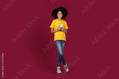 Happy adorable black preteen girl using smartphone © Prostock-studio