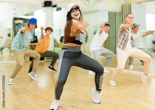 Emotional brunette teen b-girl dancing with group of friends in dance studio. Hip-hop generation.