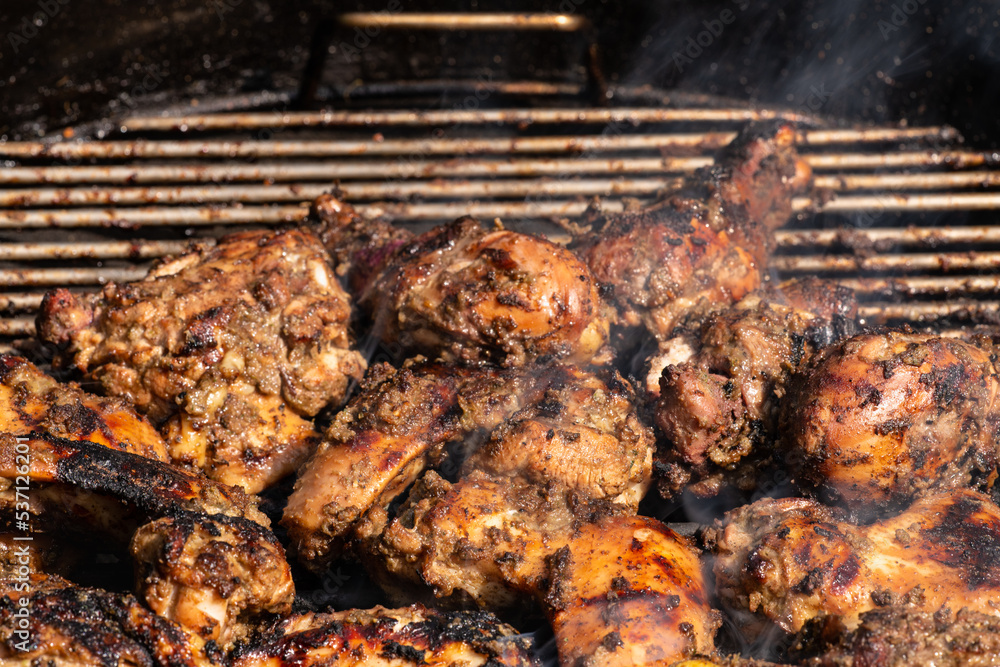 Grilling traditional Jamaican spicy jerk chicken with over charcoal fire.