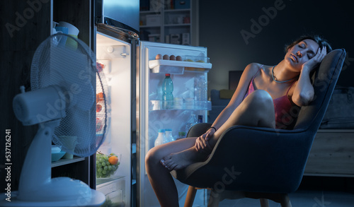Foto Woman suffering from the heat and sitting in front of the open fridge