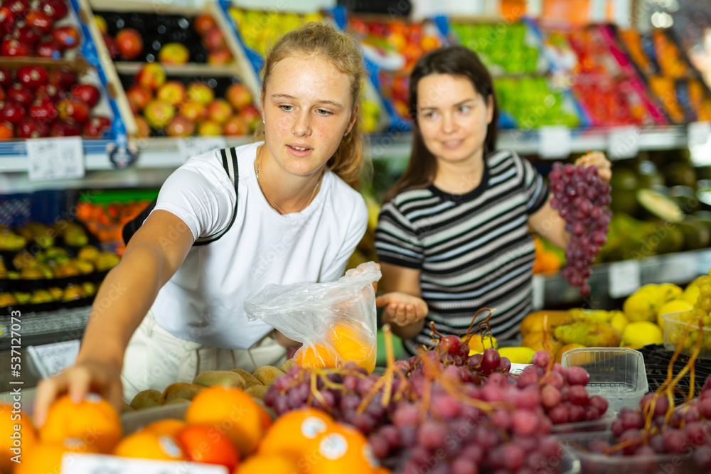 Young woman with a fifteen-year-old girl who came to the supermarket for shopping, choose fruits at the counter
