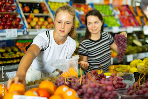 Young woman with a fifteen-year-old girl who came to the supermarket for shopping, choose fruits at the counter