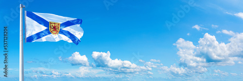 Nova Scotia - Canada flag waving on a blue sky in beautiful clouds - Horizontal banner
