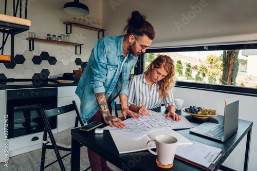 Happy couple using laptop and looking into blueprints of their new home