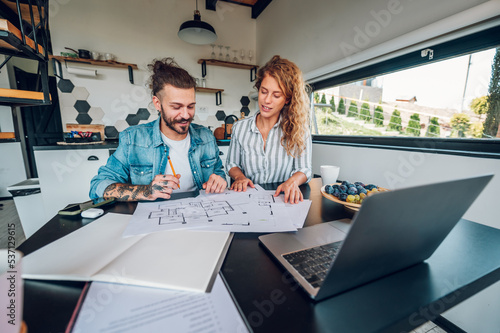 Фотография Happy couple using laptop and looking into blueprints of their new home
