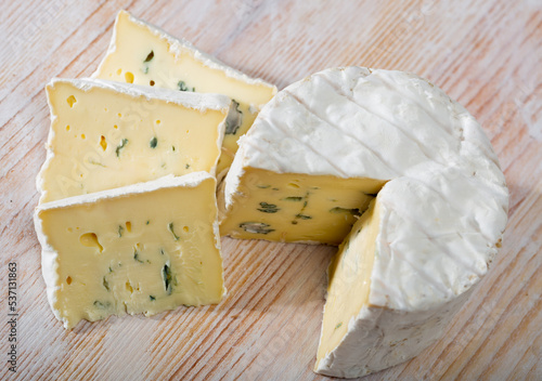 Sliced wheel of natural blue cheese with creamy structure on wooden background