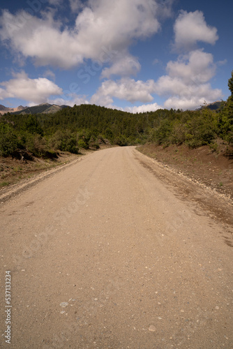 Driving along the dirt road across the mountains and forest in a sunny day. 