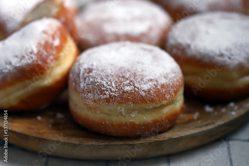 Berliner donuts in powdered sugar on a wooden tray.