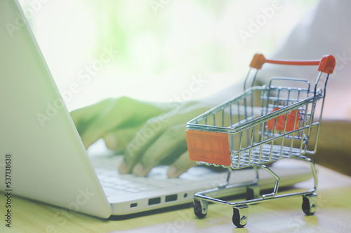 hand typing laptop with shopping cart  on wooden table.