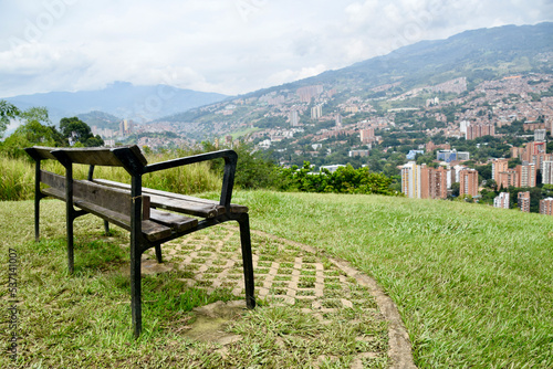 wooden bench on green grass with a city in the background  view of Medell  n from the Volador