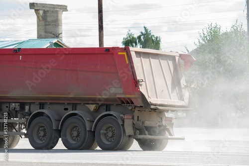 Three-axle semi-trailer heavy lifting dust moving on the road.