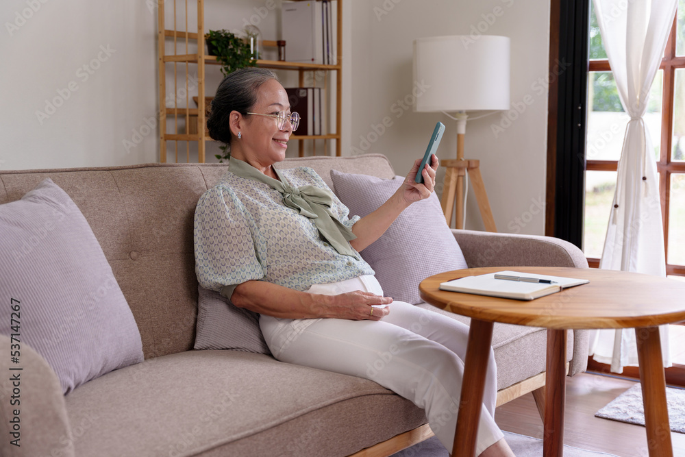 Asian senile woman relaxing at home using mobile phone in living room playing social media on vacation. Asian senile woman relaxing at home using mobile phone in living room playing social media on vacation.
